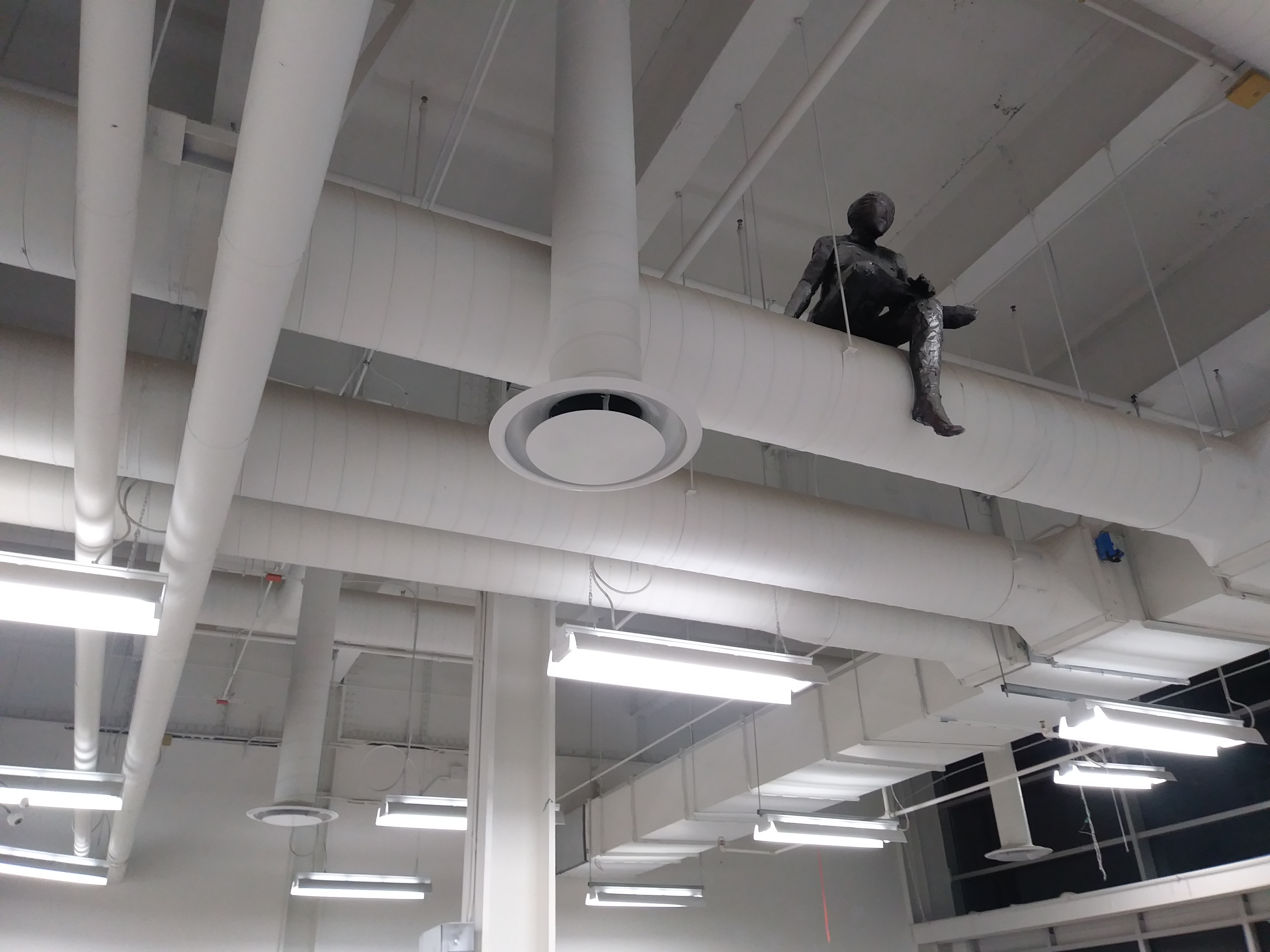 a sculpture made by Ada Denil of a human sitting on a vent in an industrial space