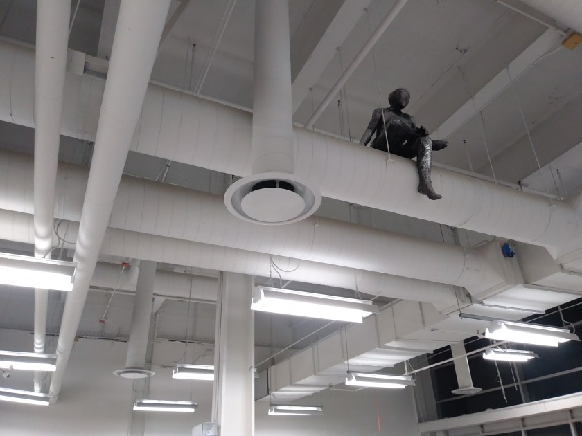 a sculpture made by Ada Denil of a human sitting on a vent in an industrial space