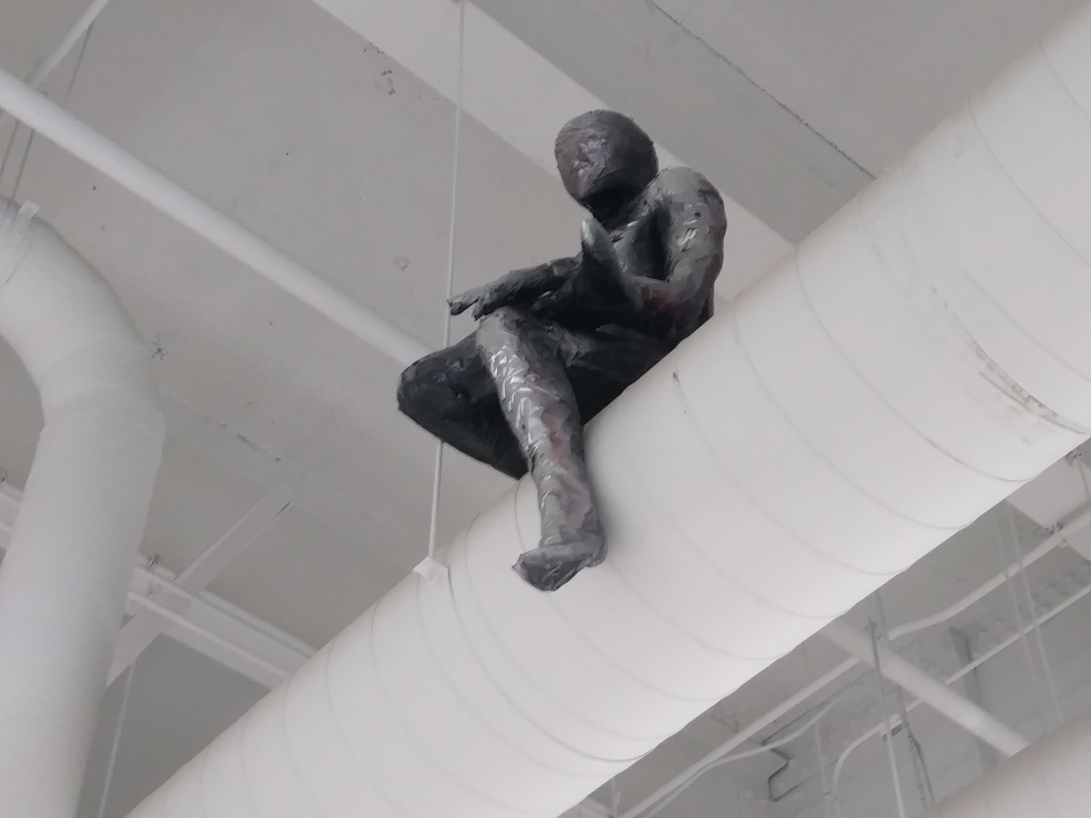 a sculpture made by Ada Denil of a human sitting on a vent in an industrial space